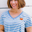 A woman smiling and wearing an off-white and blue striped t-shirt with a deep v-neckline and a small graphic on the chest.
