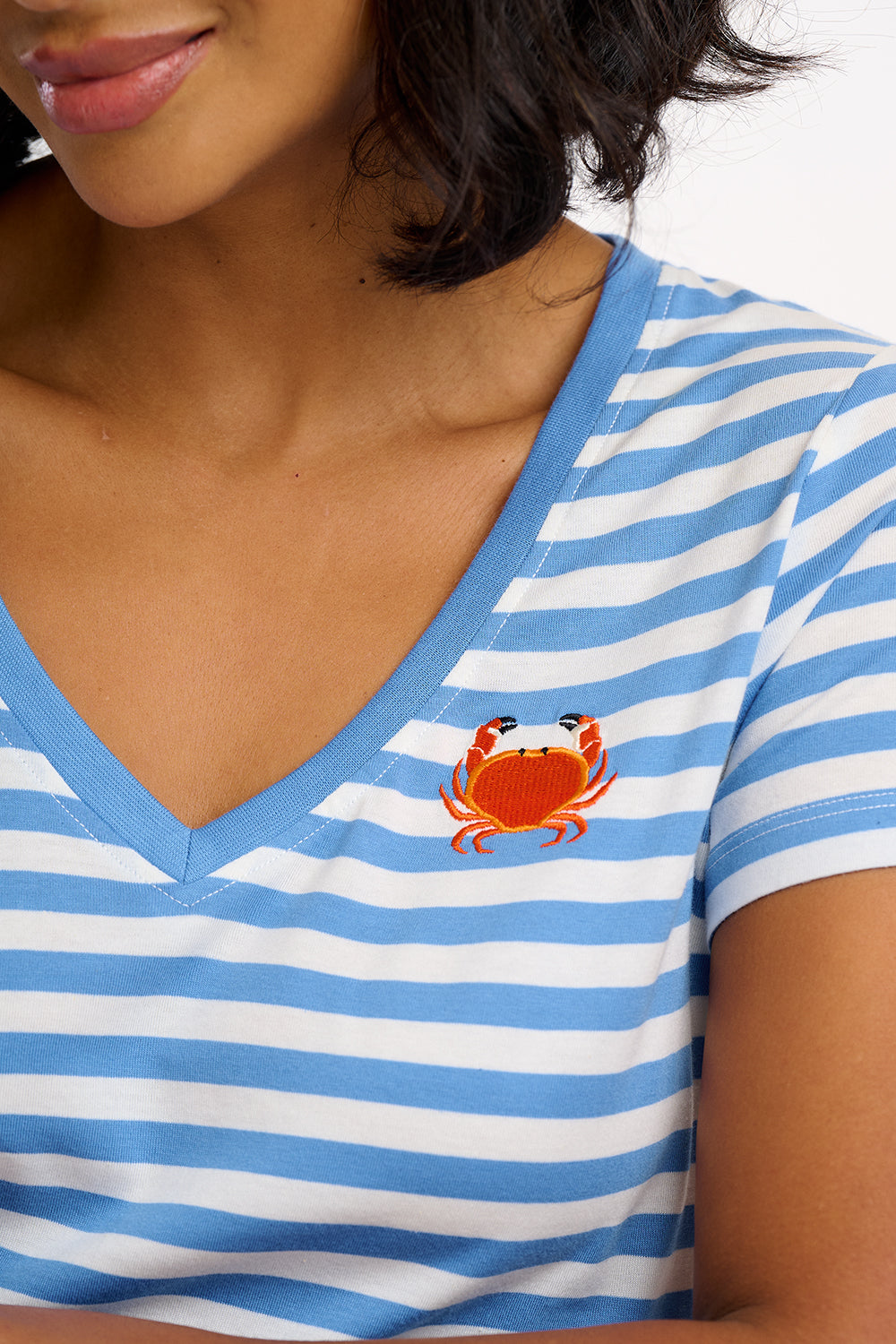 A striped V-neck t-shirt in pastel blue and white, with a small graphic of a crab on the front.