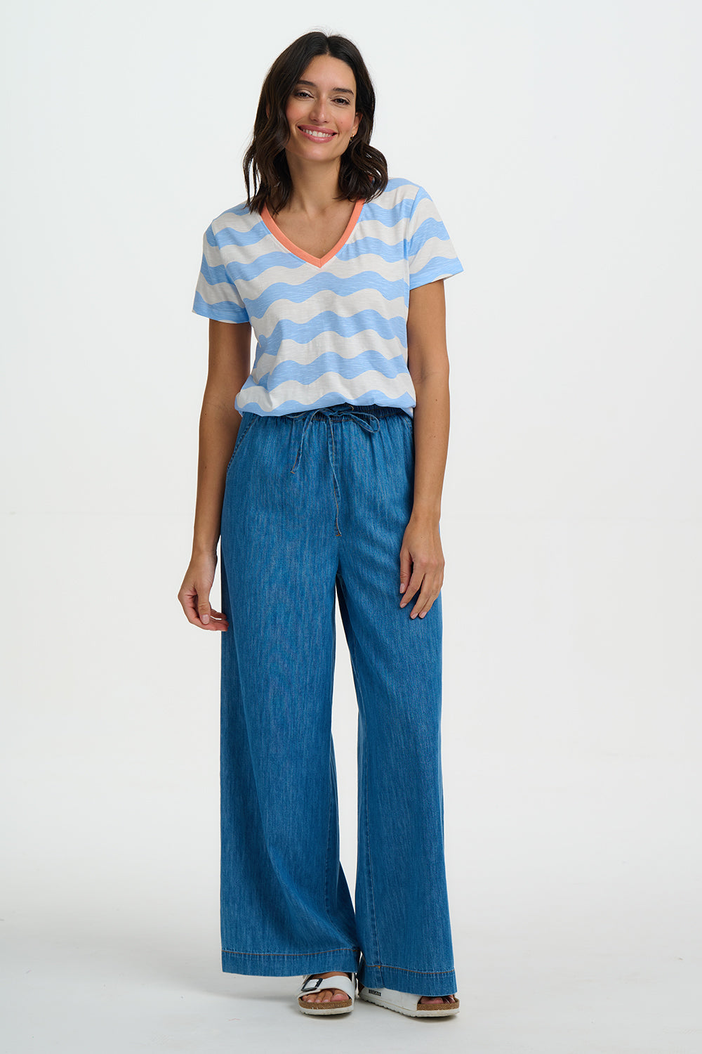Woman wearing a striped shirt and blue wide-leg pants on a white background