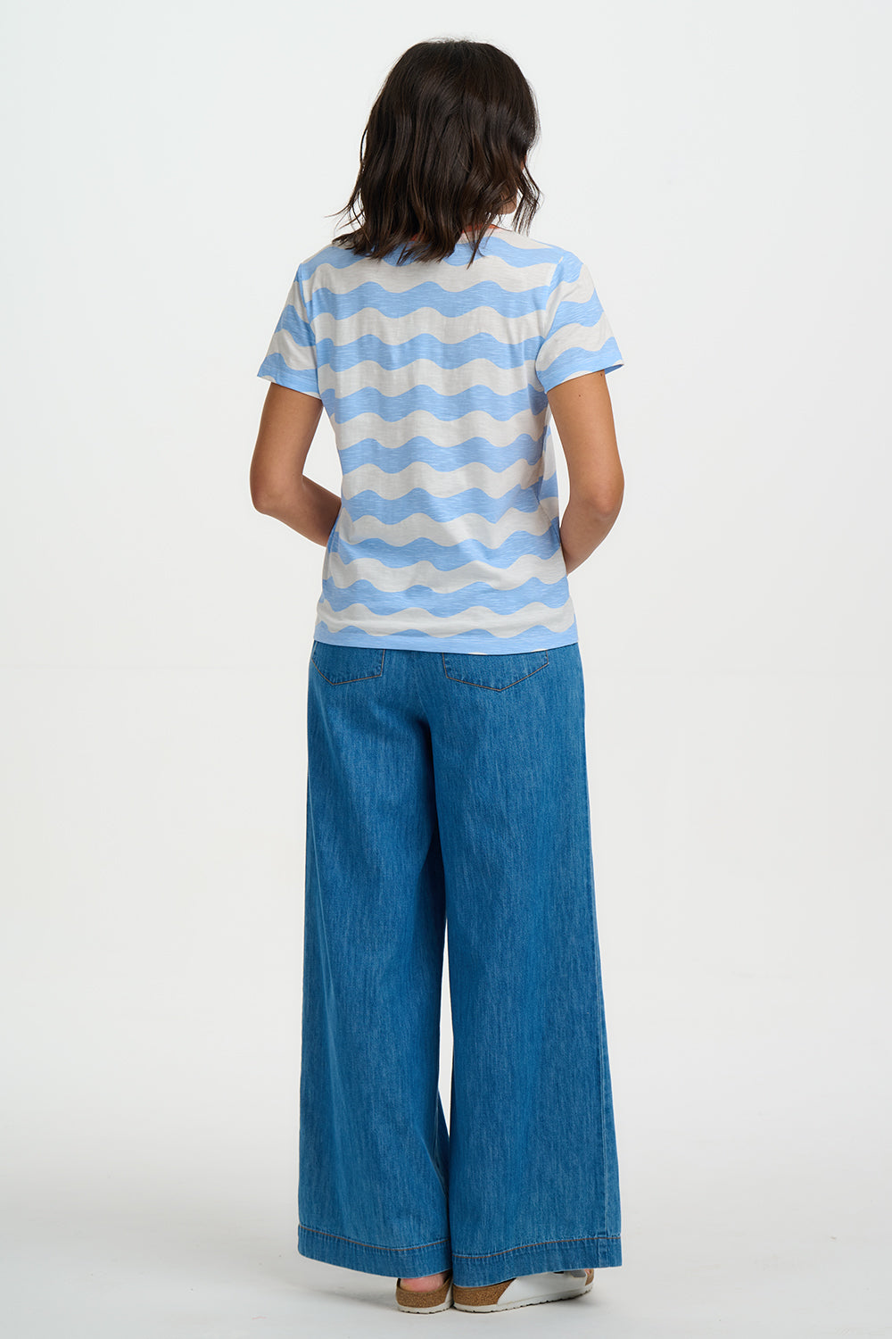Person wearing a blue and white striped shirt and blue jeans on a white background