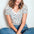 A woman sitting cross-legged and wearing a beige V-neck T-shirt with a multicolor polka dot pattern, paired with blue jeans.
