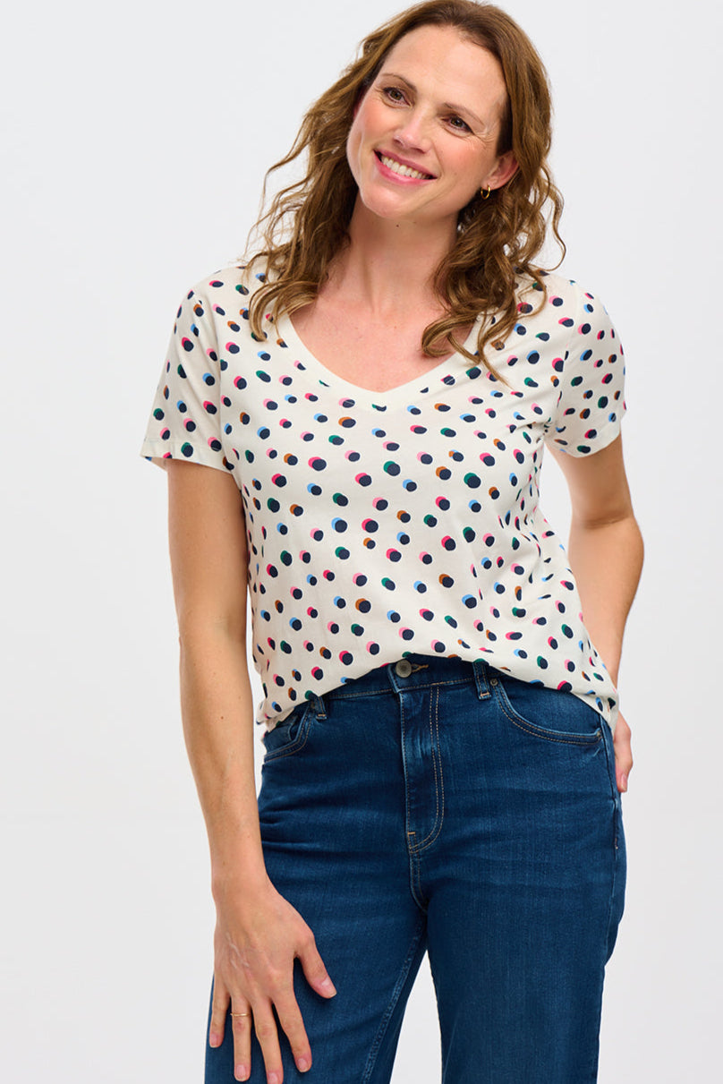 A wearing a beige V-neck T-shirt with a multicolor polka dot pattern, paired with blue jeans.
