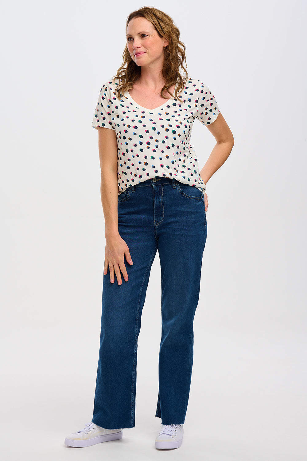 A wearing a beige V-neck T-shirt with a multicolor polka dot pattern, paired with blue jeans.