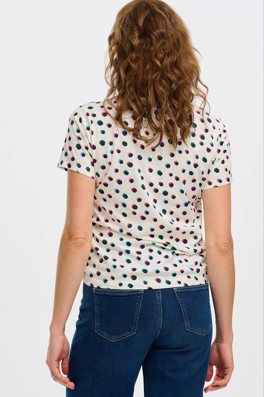 A wearing a beige V-neck T-shirt with a multicolor polka dot pattern, paired with blue jeans.