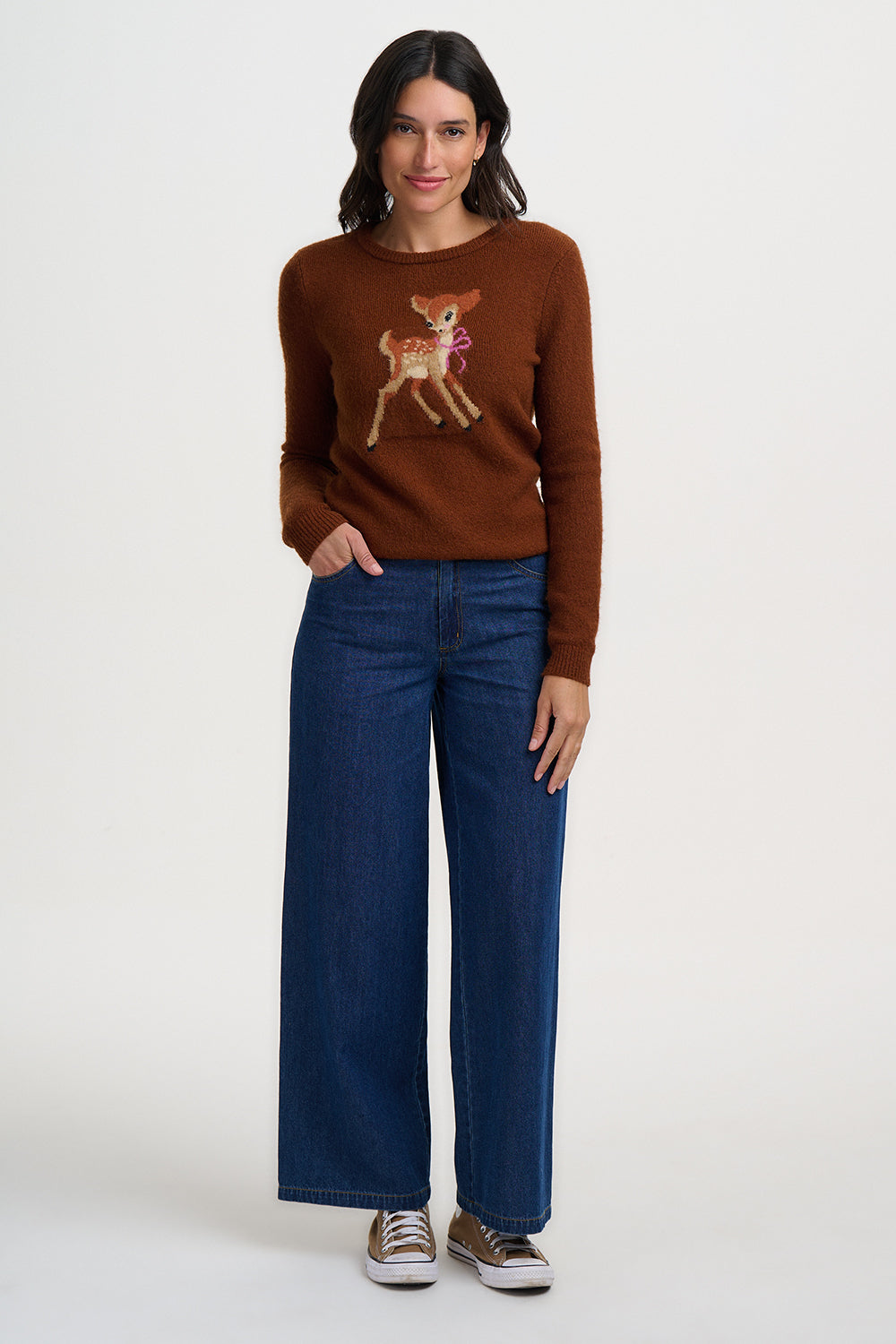 Woman wearing a brown sweater with a deer design and blue jeans on a white background