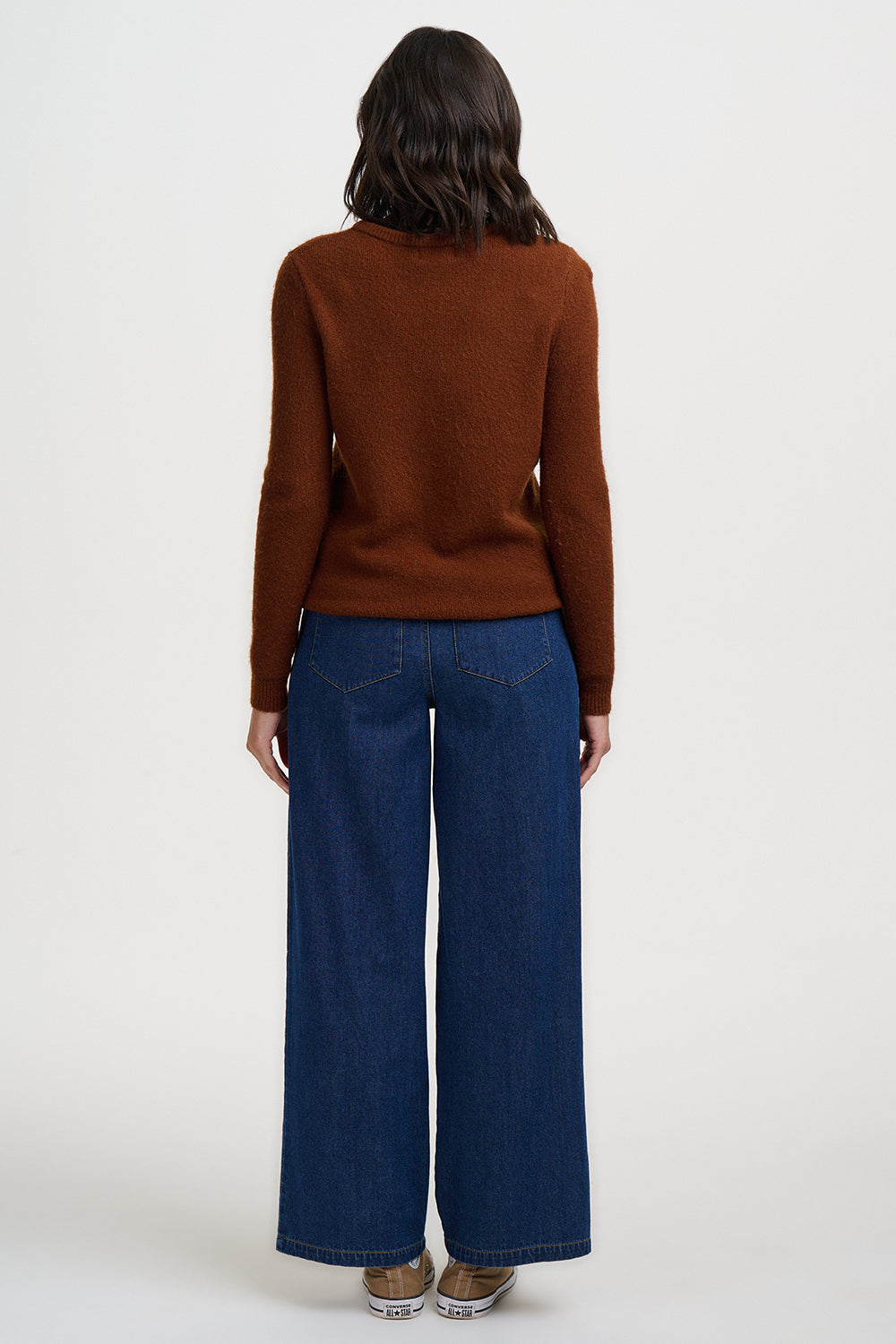 Person wearing a brown sweater and blue jeans on a white background
