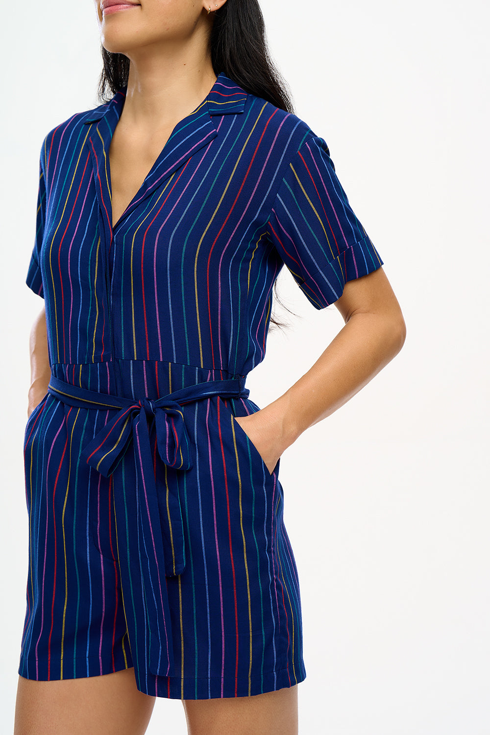 A navy playsuit with thin rainbow stripes, featuring a V-neck shirt collar, button-down front, and a tie belt.