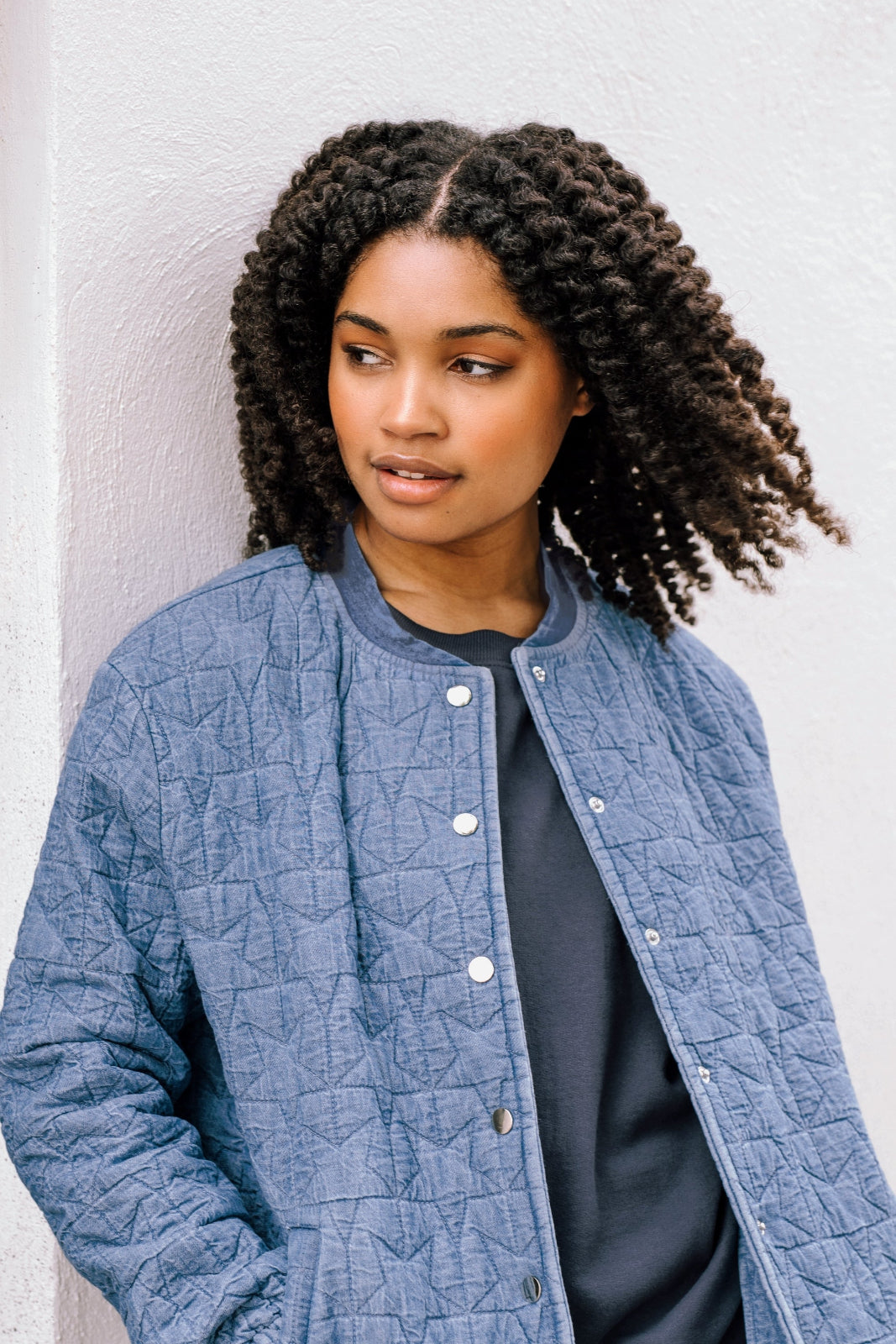 A woman wearing a light blue denim quilted bomber jacket with star quilt pattern, featuring a crew neck, popper front fastening, and elasticated back hem and cuffs.