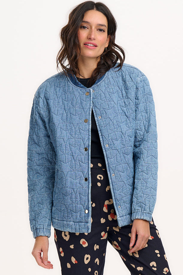 A woman wearing a light blue denim quilted bomber jacket with star quilt pattern, featuring a crew neck, popper front fastening, and elasticated back hem and cuffs.