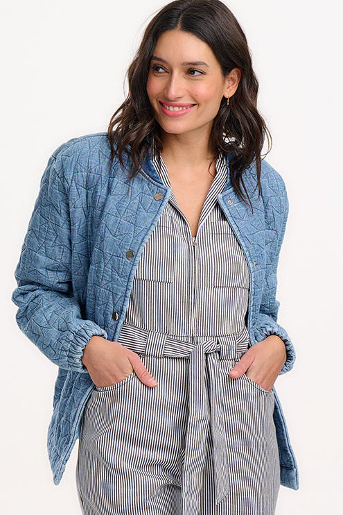 A woman wearing a light blue denim quilted bomber jacket with star quilt pattern, featuring a crew neck, popper front fastening, and elasticated back hem and cuffs.