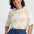 Woman wearing a white shirt with yellow sun patterns and blue pants on a light gray background