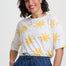 Woman wearing a white shirt with yellow sun patterns and blue pants on a light gray background