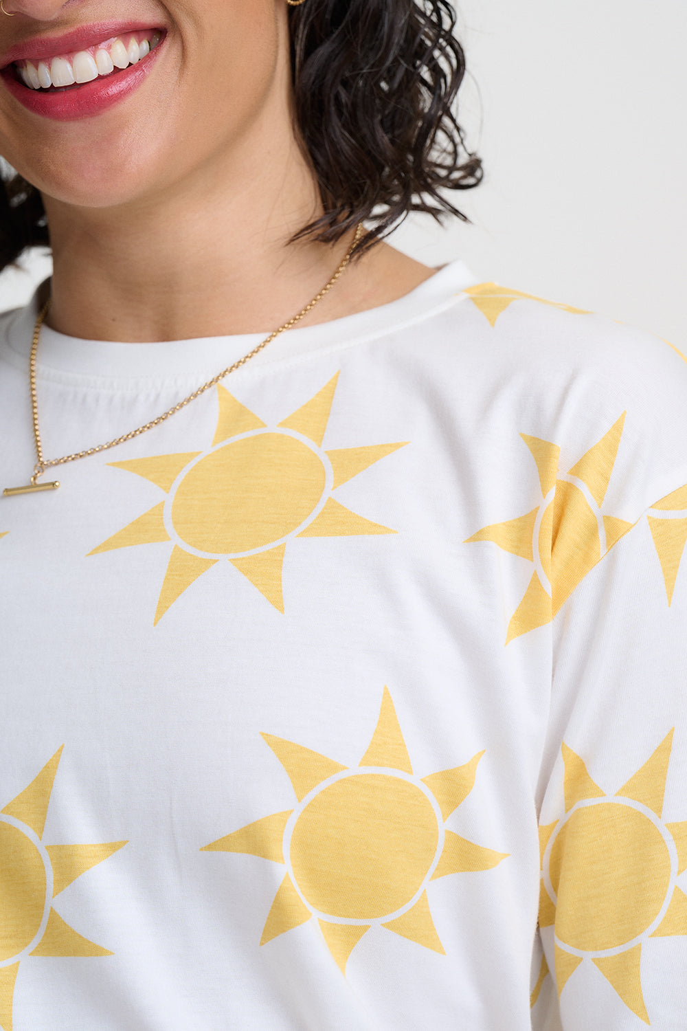 Person wearing a white sweater with yellow sun patterns on a plain background