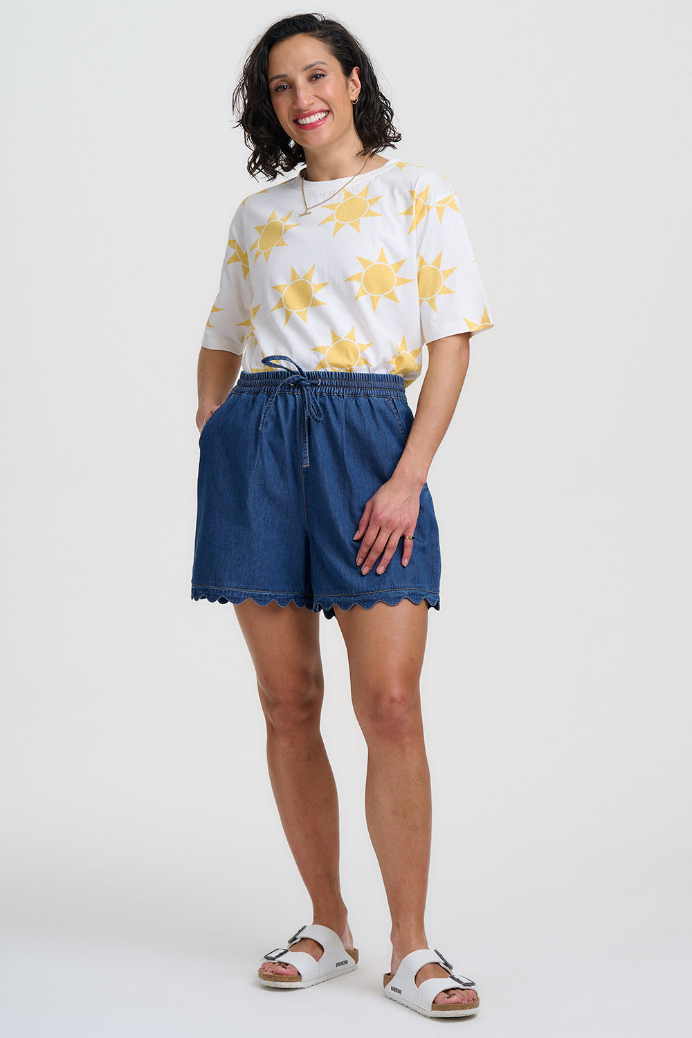 Woman wearing a white shirt with yellow floral patterns and blue shorts on a white background