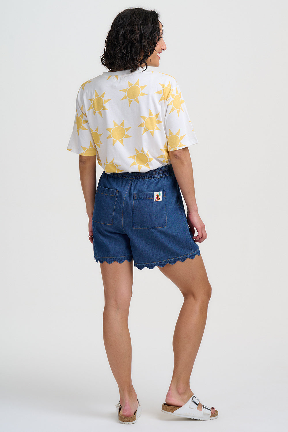 Person wearing a white shirt with yellow star patterns and blue shorts on a white background