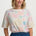 Woman wearing a colorful patterned shirt with blue pants on a white background