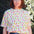 A person wearing a white relaxed fit t-shirt with a fruit salad print, including various colorful fruits such as strawberries and grapes, paired with blue denim shorts.