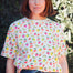 A person wearing a white relaxed fit t-shirt with a fruit salad print, including various colorful fruits such as strawberries and grapes, paired with blue denim shorts.