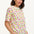 A woman smiling and wearing a cream-colored short-sleeved t-shirt with a fruit salad print.