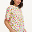 A woman smiling and wearing a cream-colored short-sleeved t-shirt with a fruit salad print.