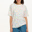 A woman modeling an oversized white t-shirt with a colorful sprinkle print, paired with denim shorts.