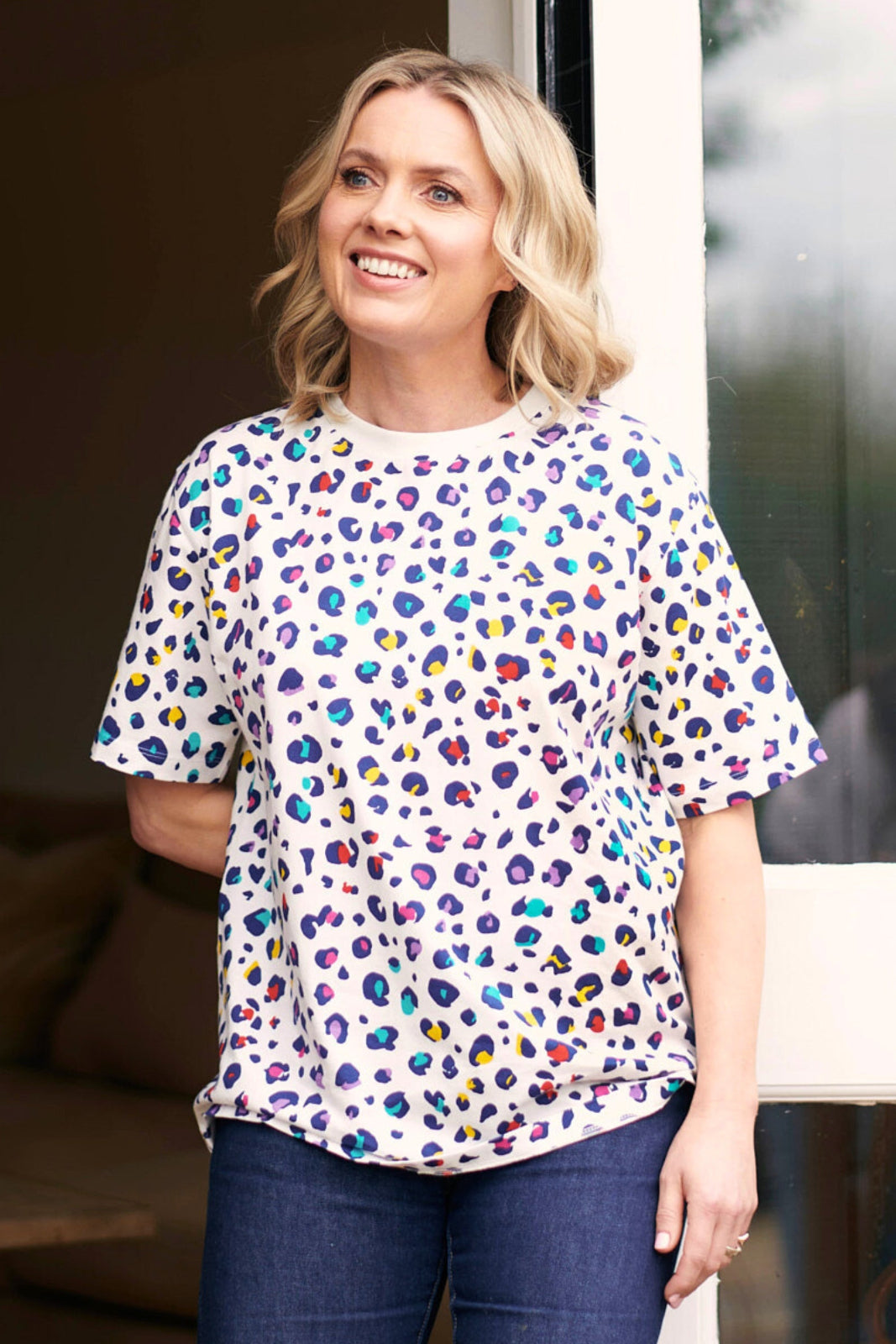 A woman wearing an oversized white t-shirt with a multicolored leopard print pattern, paired with blue jeans.