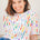 A person wearing an off-white relaxed fit t-shirt with a bold broken lines print in vibrant colors.
