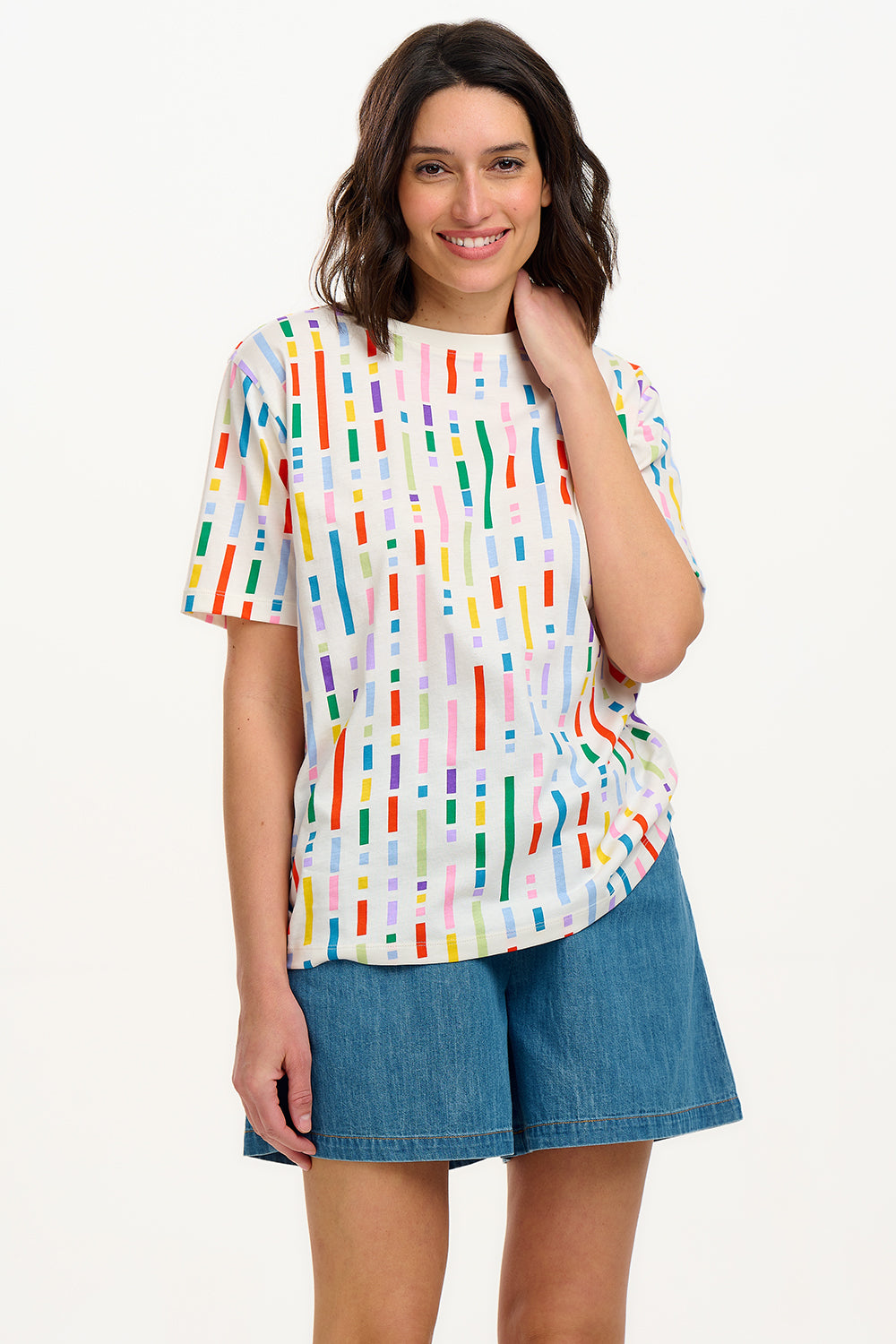 A woman smiling and wearing an oversized white t-shirt with a broken lines multicolor print, paired with denim shorts.