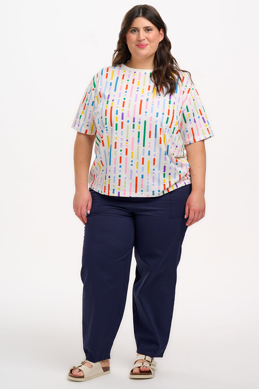 A woman smiling and wearing an oversized white t-shirt with a broken lines multicolor print, paired with denim shorts.