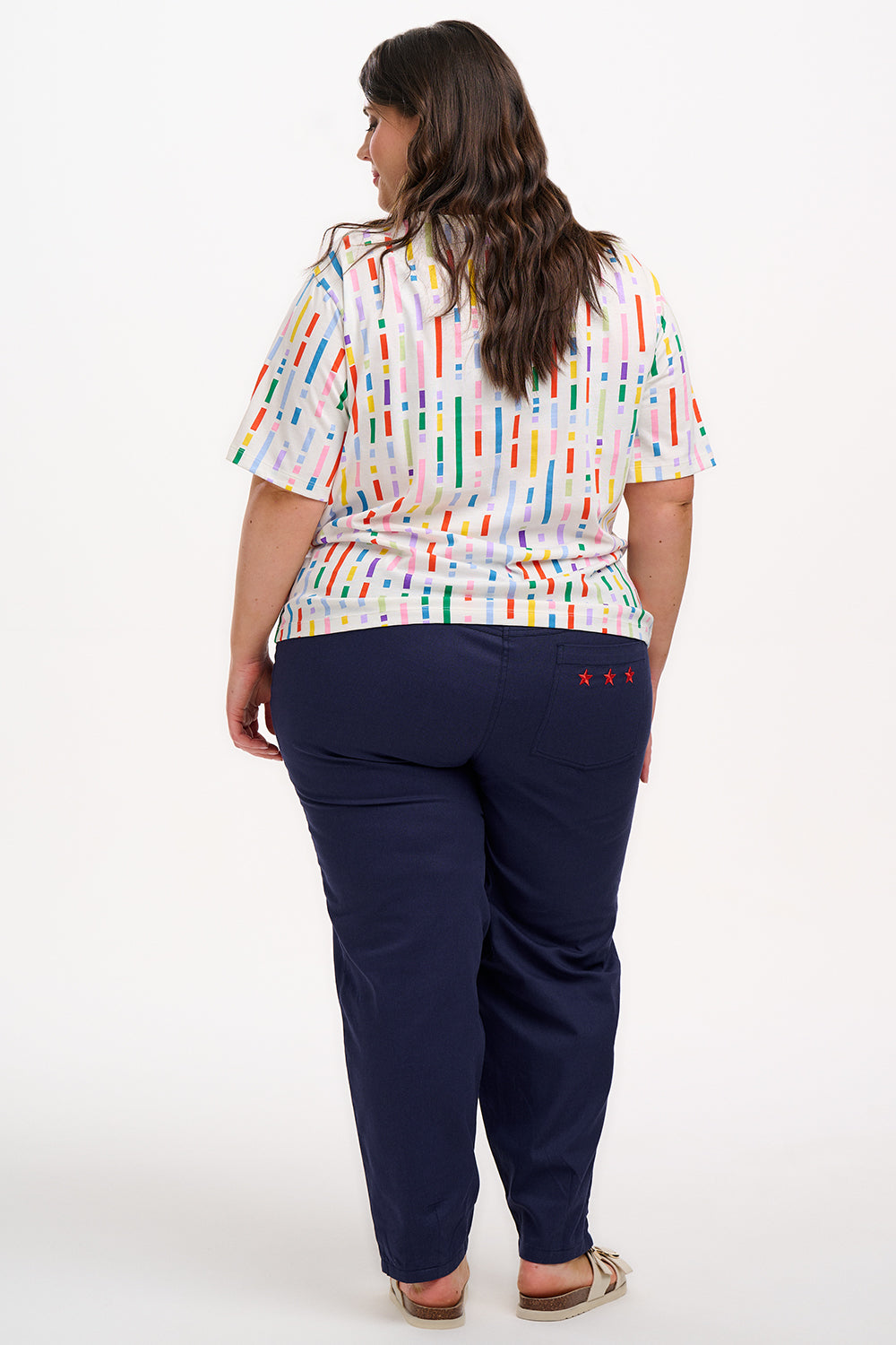 A woman smiling and wearing an oversized white t-shirt with a broken lines multicolor print, paired with denim shorts.