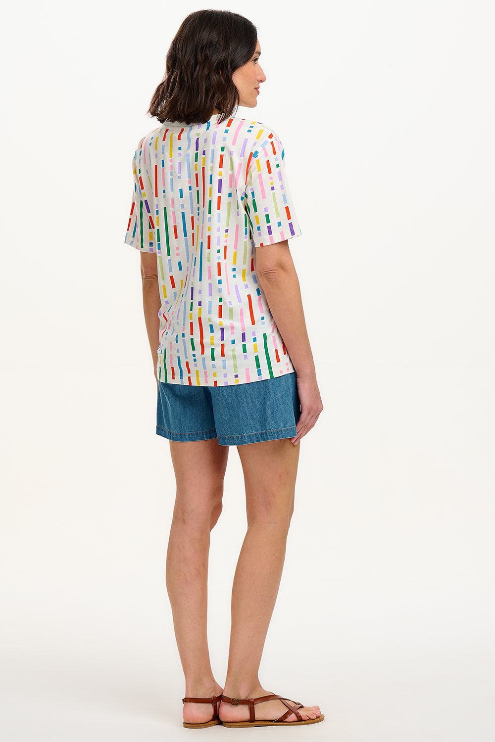 A woman smiling and wearing an oversized white t-shirt with a broken lines multicolor print, paired with denim shorts.