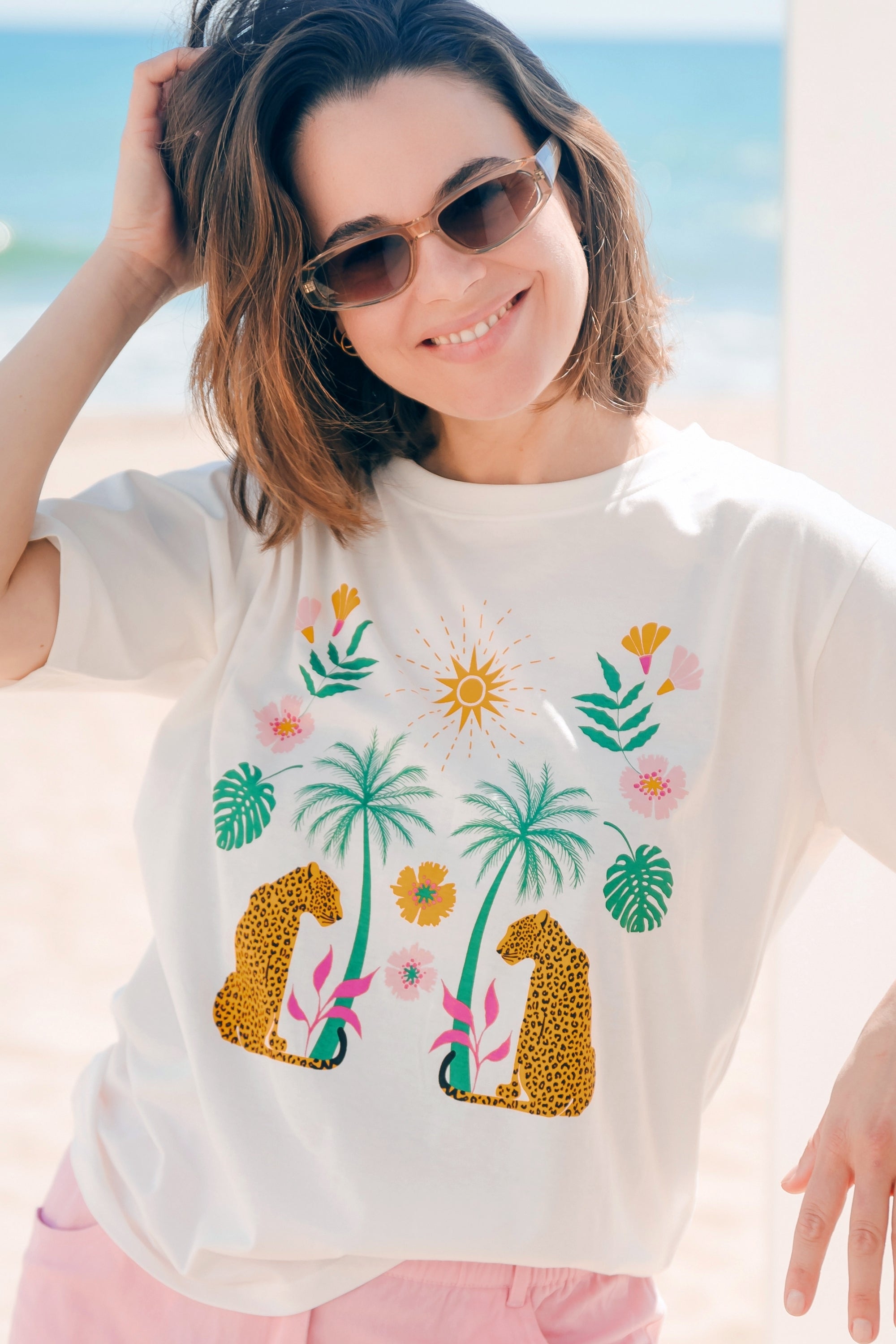 Woman wearing a white t-shirt with palm tree and leopard designs at the beach.
