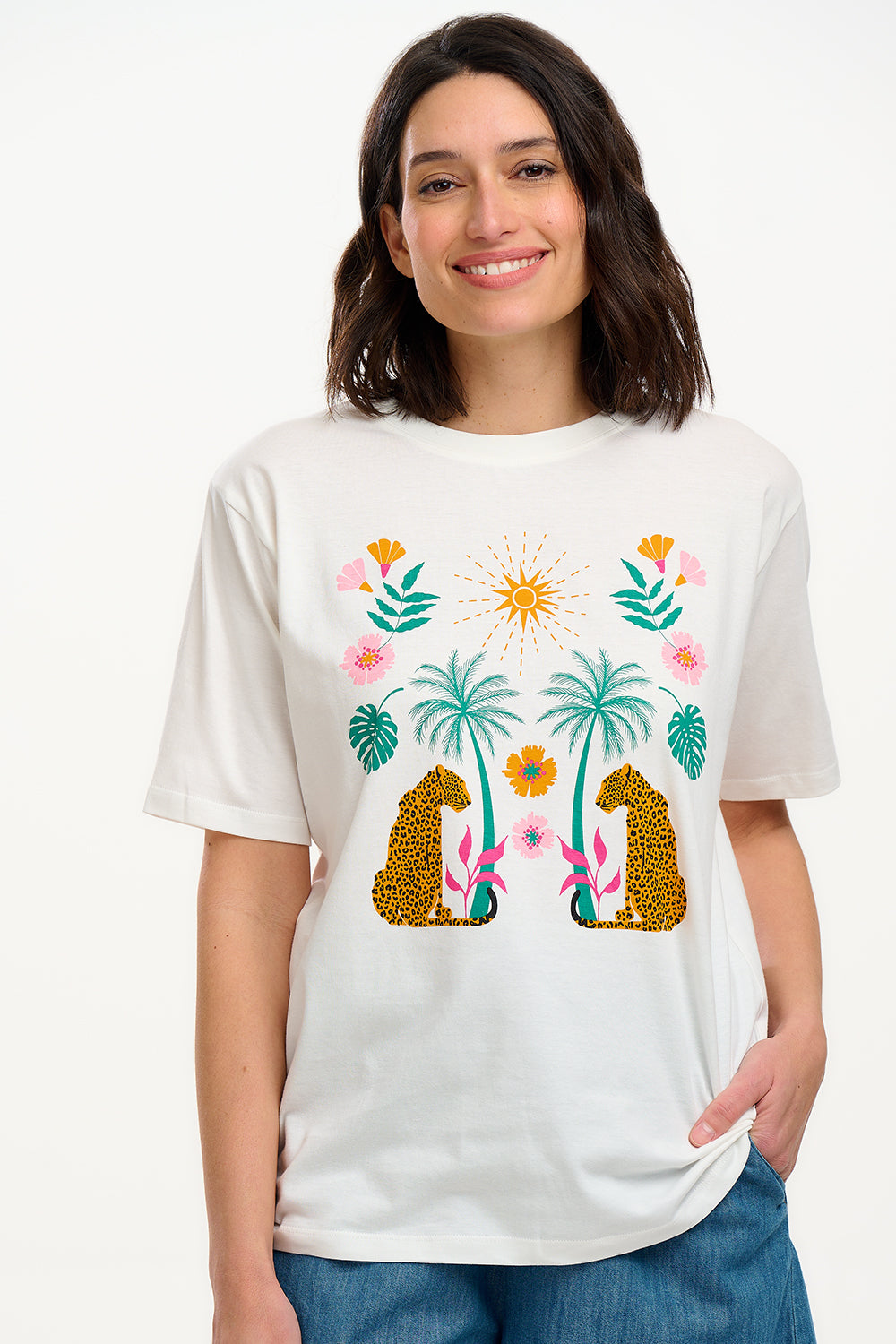 A woman smiling and wearing an off-white colored t-shirt with a mirrored jungle print design, featuring palm trees, leopards, and flowers.