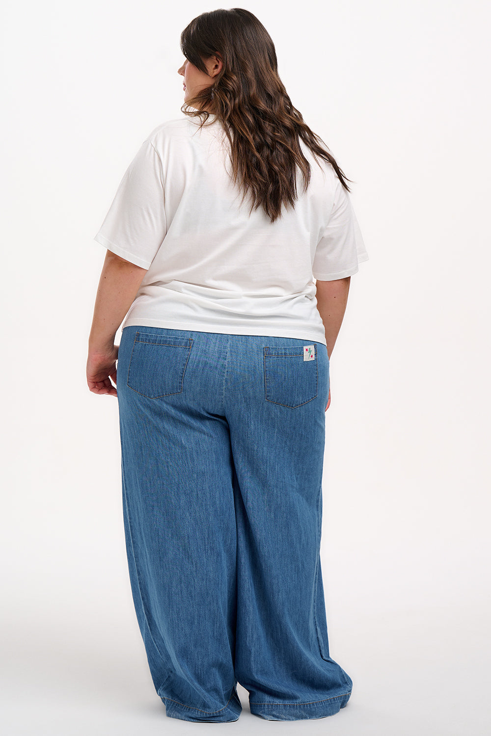 A woman smiling and wearing an off-white colored t-shirt with a mirrored jungle print design, featuring palm trees, leopards, and flowers.