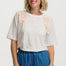 Woman wearing a white t-shirt with floral embroidery and blue pants on a white background