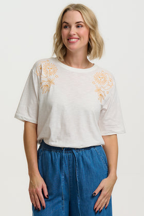 Woman wearing a white t-shirt with floral embroidery and blue pants on a white background