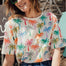 A woman smiling and wearing a relaxed fit t-shirt with a colorful palm tree print.