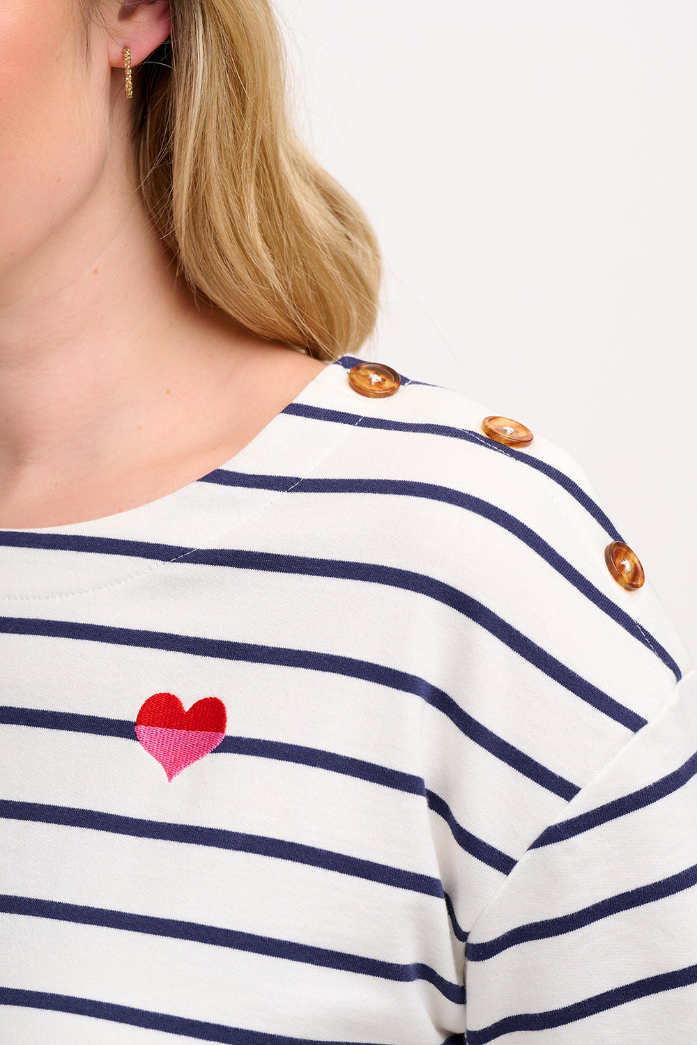 A woman wearing an off-white and navy striped short-sleeved t-shirt with a small embroidered red and pink heart on the chest.