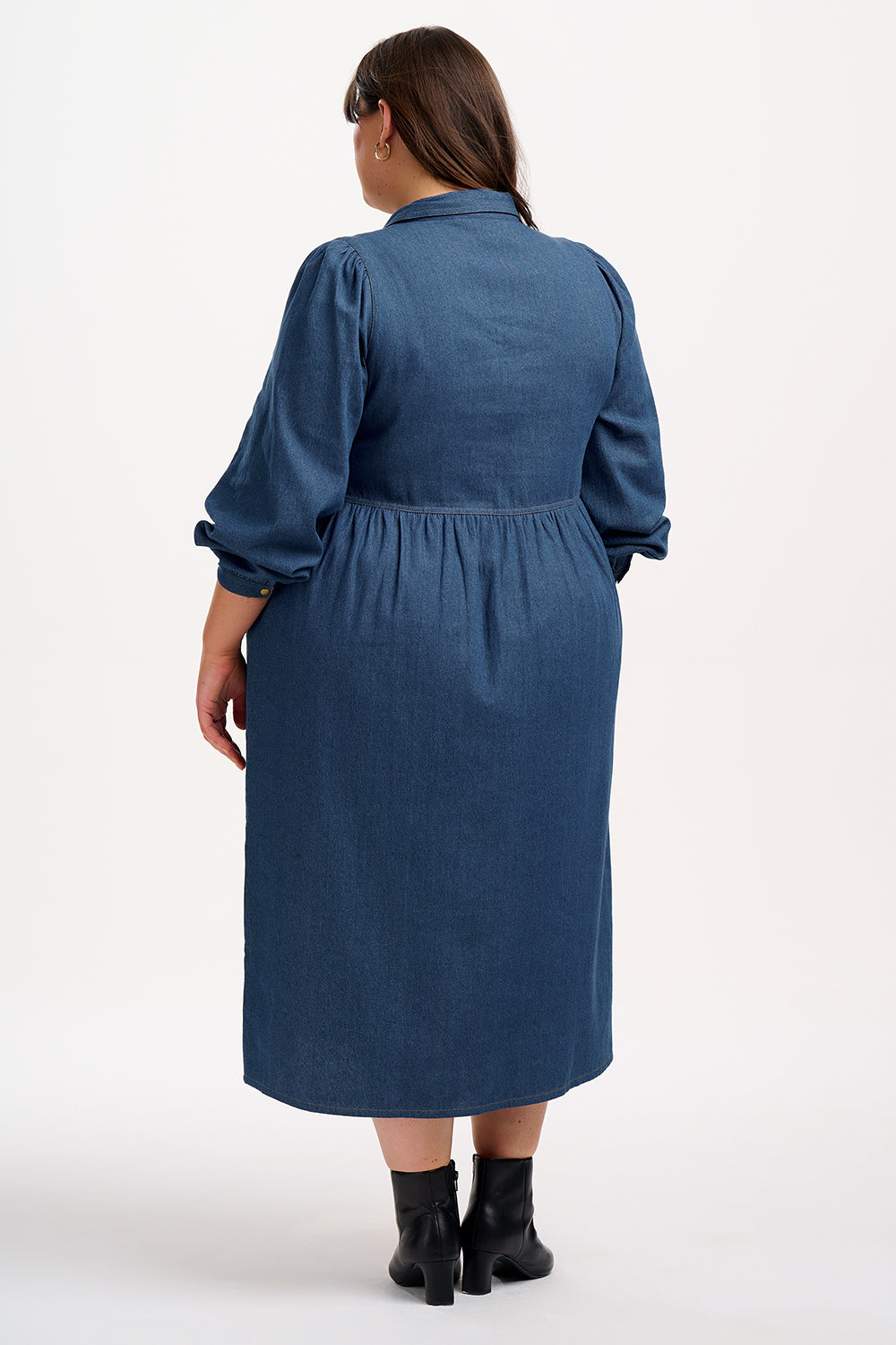 A mid-length denim smock dress with a front zip fastening and cuffed sleeves, worn by a model posing against a white background.