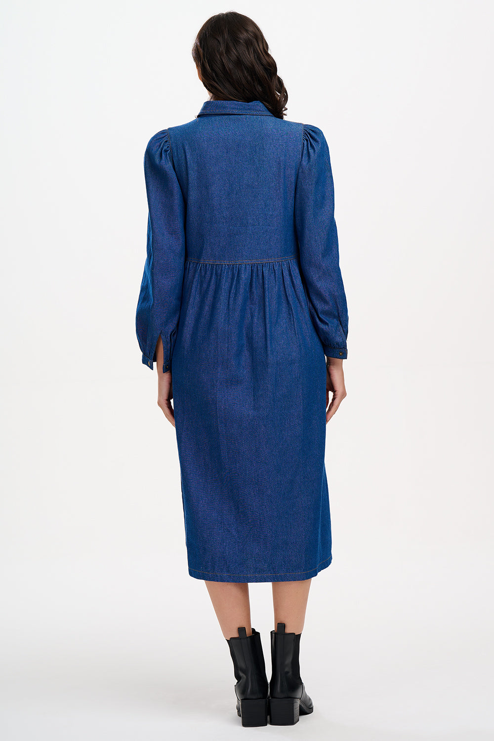 A mid-length denim smock dress with a front zip fastening and cuffed sleeves, worn by a model posing against a white background.