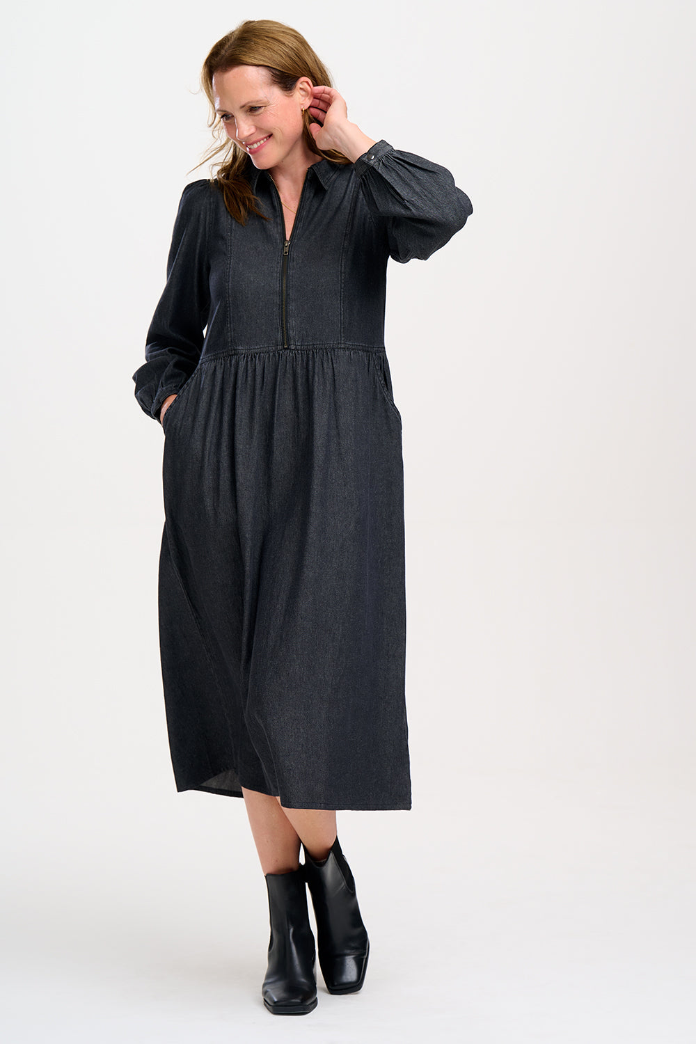 A woman standing and posing in a washed black midi smock dress with exposed zip fastening at the front and blouson cuffed sleeves.