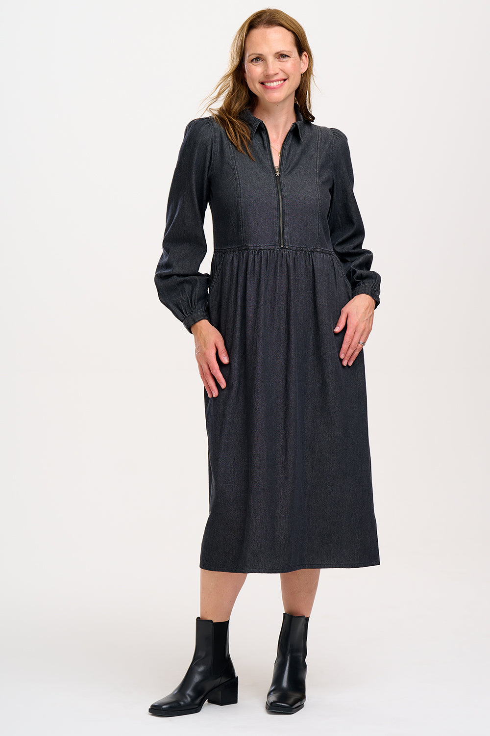 A woman standing and posing in a washed black midi smock dress with exposed zip fastening at the front and blouson cuffed sleeves.