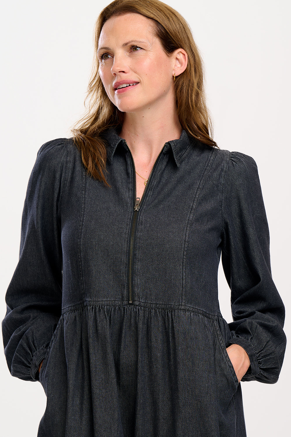 A woman standing and posing in a washed black midi smock dress with exposed zip fastening at the front and blouson cuffed sleeves.