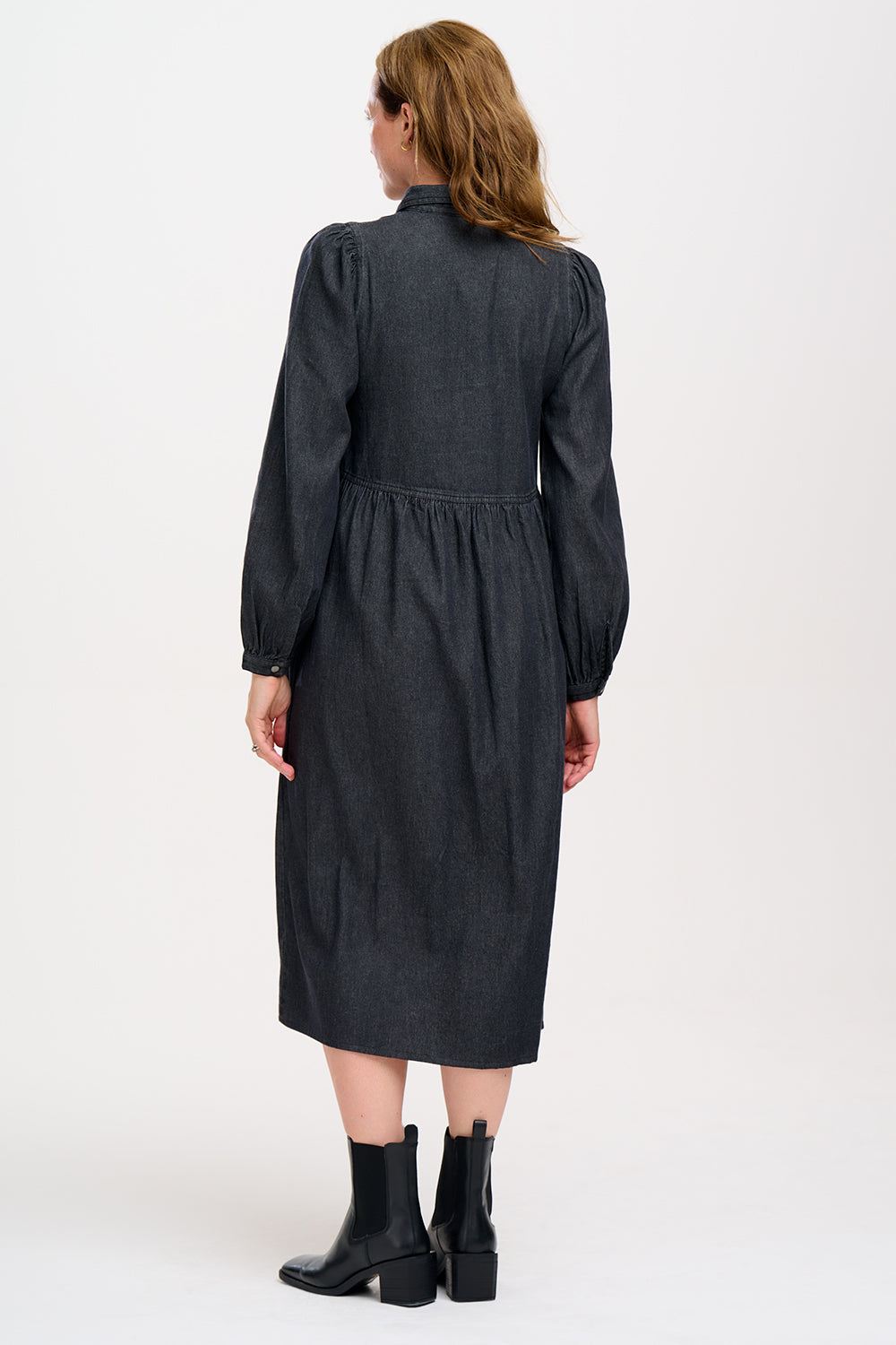 A woman standing and posing in a washed black midi smock dress with exposed zip fastening at the front and blouson cuffed sleeves.