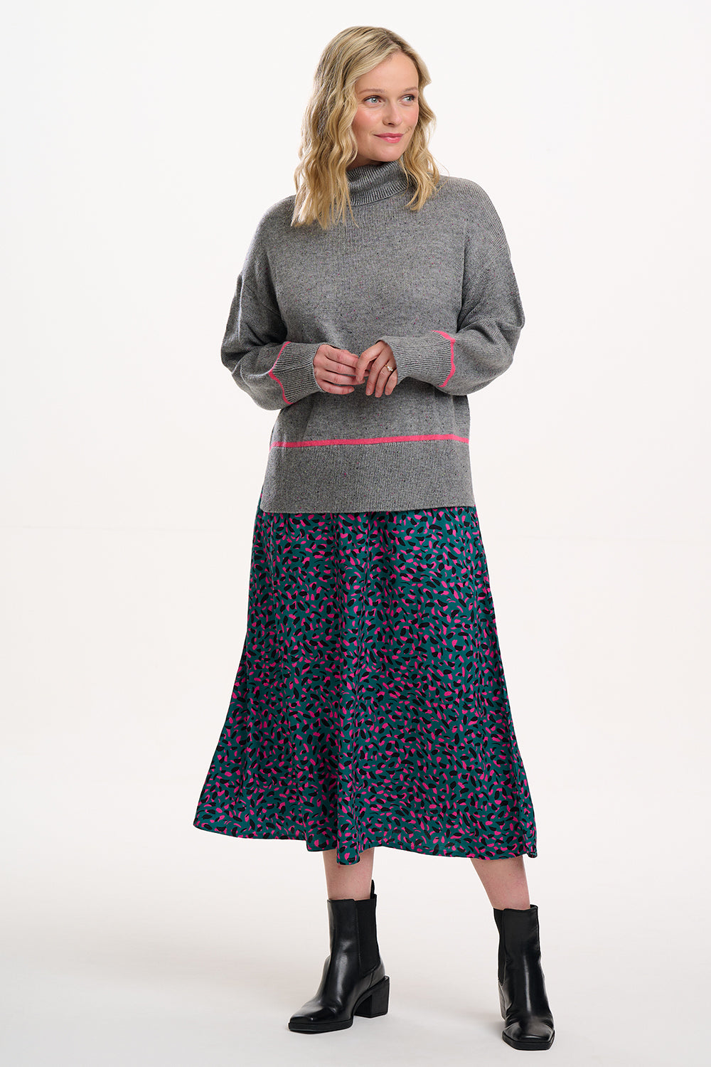 Woman wearing a gray sweater with pink trim and a patterned skirt on a white background