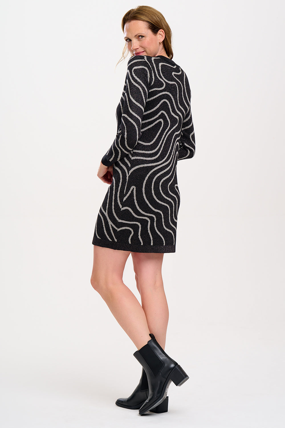 A woman wearing a long sleeve, mini knit dress with a crew neckline featuring gunmetal and silver swirls.