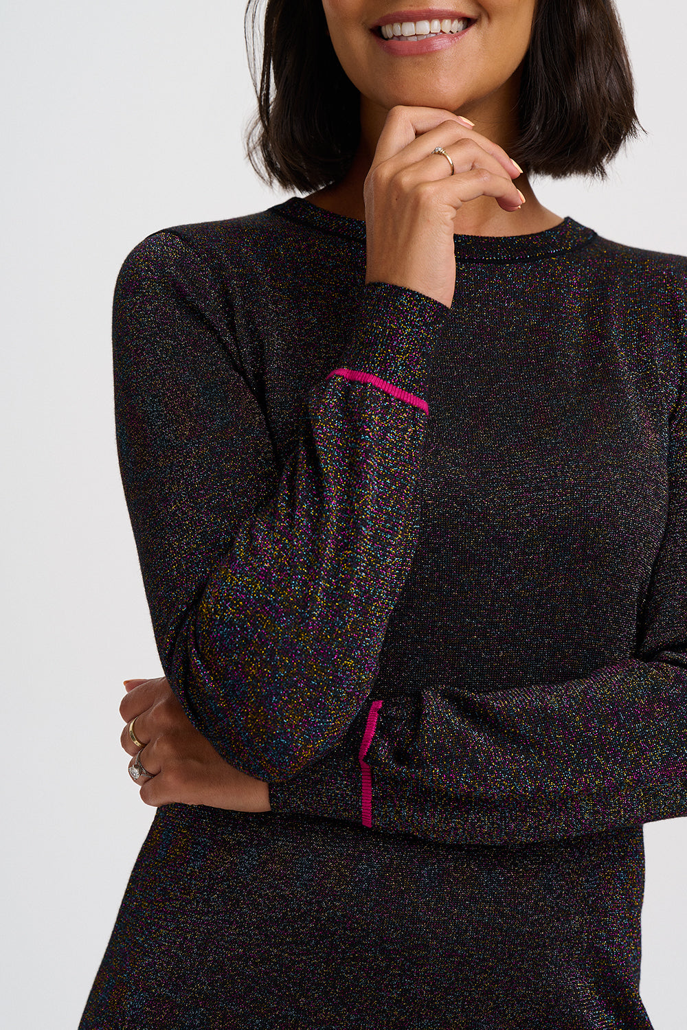 A woman wearing a dark multicolor speckled long-sleeve top with bright pink contrast stitching on the cuffs, shown against a light gray studio background.