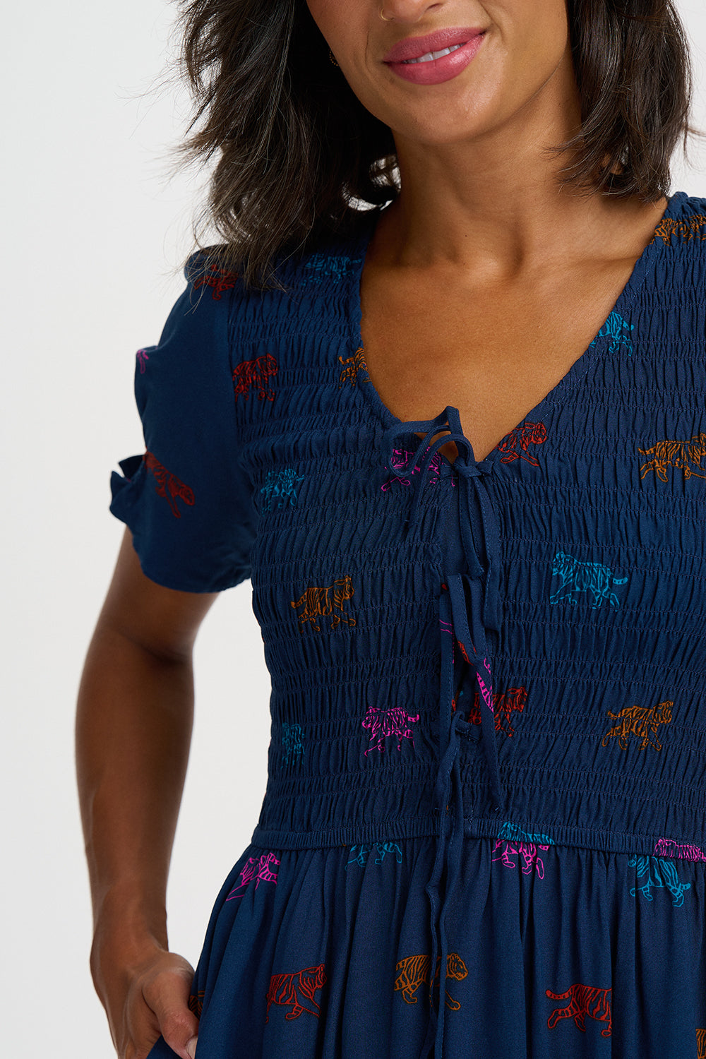 A close-up of a woman wearing a navy blue smocked dress with colorful embroidered butterfly details, featuring a tie-neck and short puff sleeves.