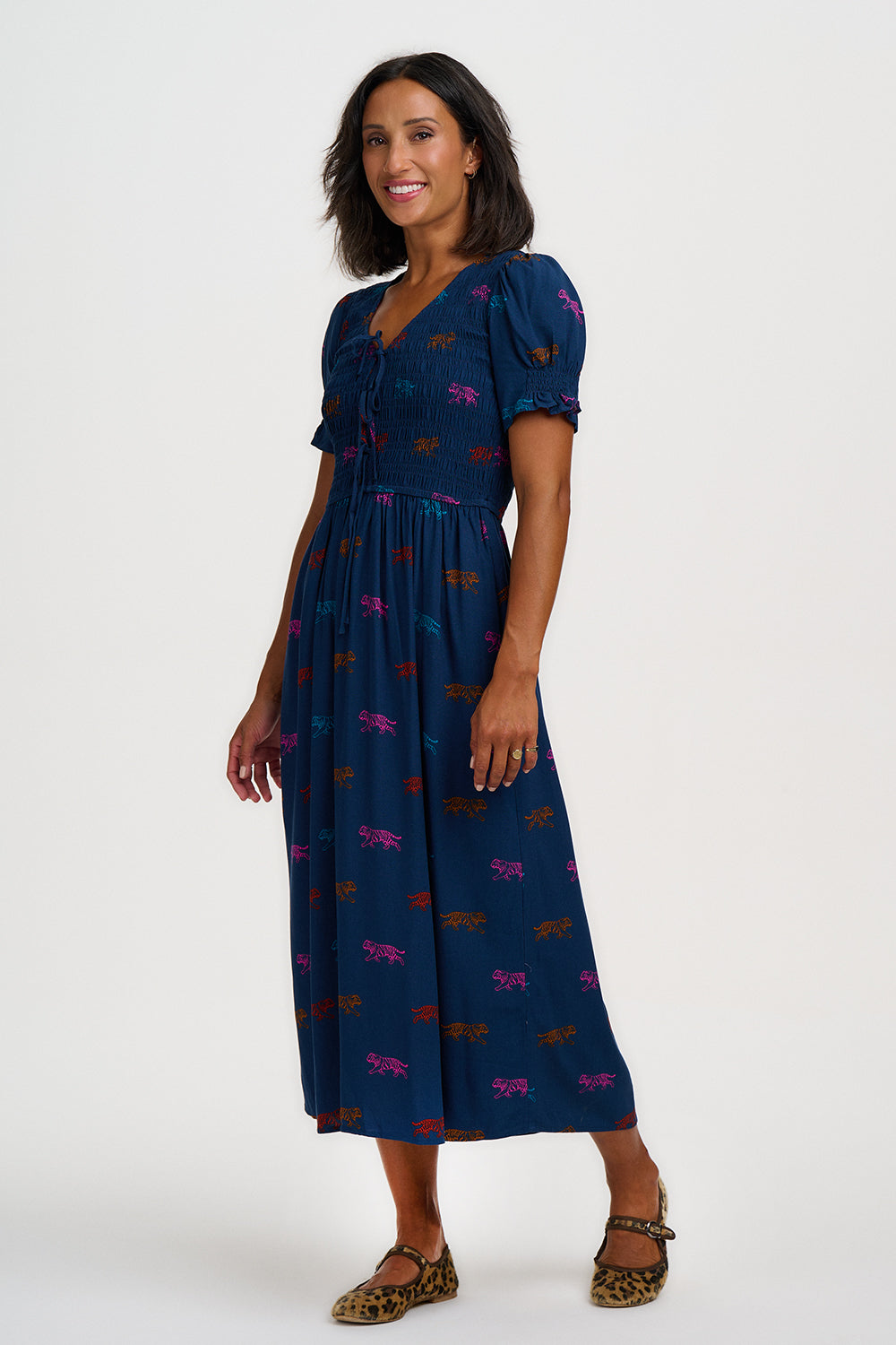 A woman modeling a navy blue midi dress with puff sleeves and a colorful animal print, paired with leopard-print flat shoes, against a plain light gray background.