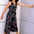 A woman modeling a sleeveless black jumpsuit with a v-neck and retro geometric print, standing against a wall.